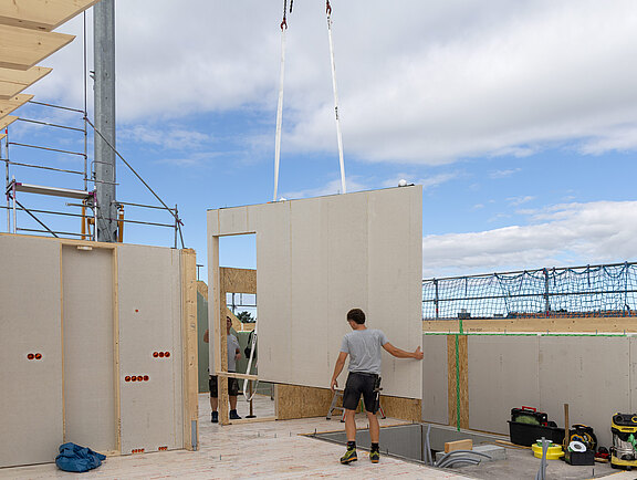 Montage eines vorgefertigten Wandelements beim Neubau eines mehrgeschossigen Holzhauses.