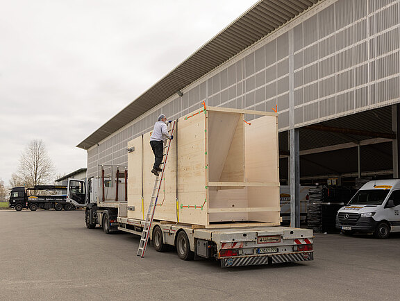 LKW-Fahrer sichert vorgefertigten Treppenturm aus Holz f&uuml;r Transport zur Baustelle.