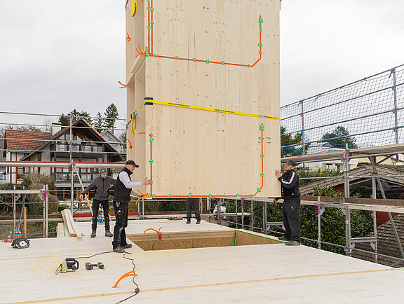 Ein Treppenturm am Kran wird von Zimmerern auf der Baustelle exakt positioniert