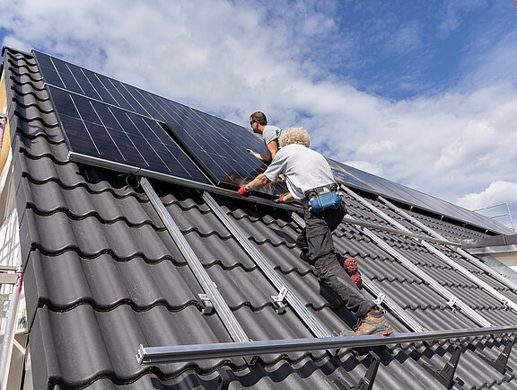 Zimmerer montieren Photovoltaikanlage auf dem Dach eines neuen Mehrfamilienhauses in Holzbauweise